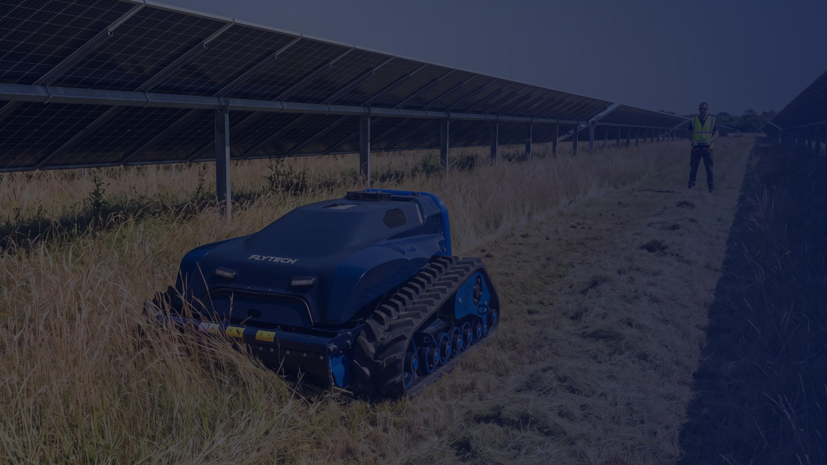 Rover cingolato al lavoro fra le file di un impianto fotovoltaico, con l’operatore che conduce da lontano